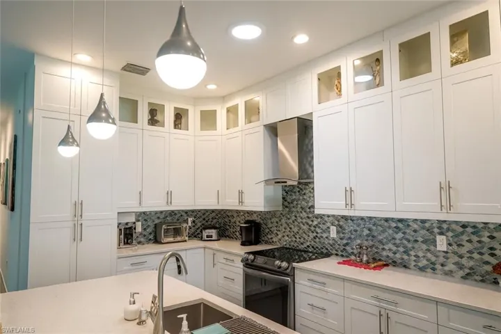 Kitchen featuring white cabinets, hanging light fixtures, range with electric cooktop, wall chimney exhaust hood, and decorative backsplash