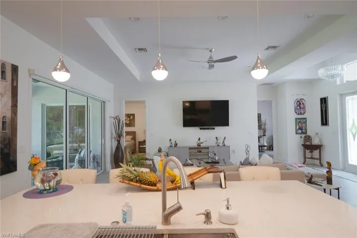 Kitchen featuring a raised ceiling, pendant lighting, light stone counters, open floor plan, and a ceiling fan