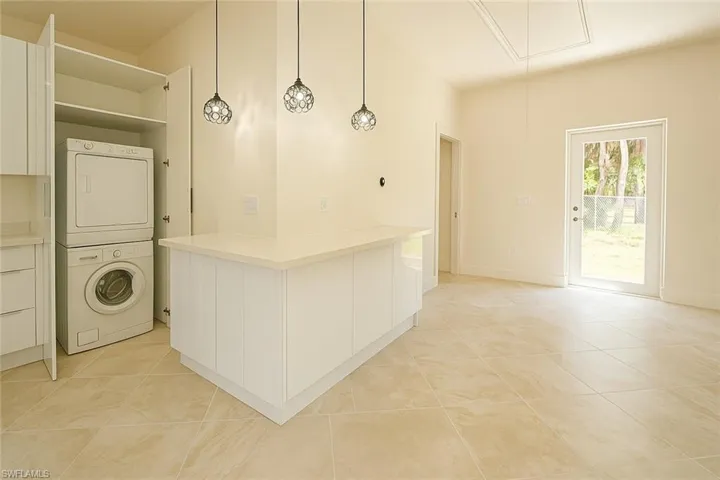 Laundry area with attic access, light tile patterned flooring, and stacked washing machine and dryer