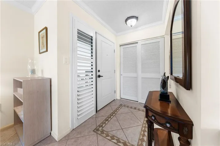 Entrance foyer with light tile patterned floors, crown molding, inlaid floor details, and a textured ceiling