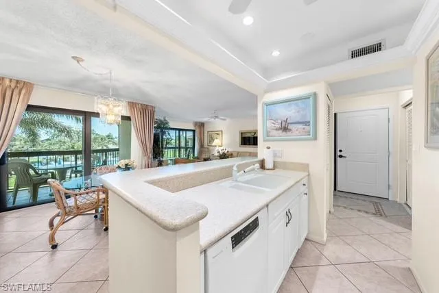 Kitchen with ceiling fan, a peninsula, dishwasher, a chandelier, and a tray ceiling