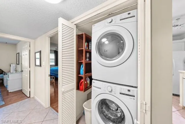 Laundry area featuring light tile patterned floors, stacked washer / dryer, and a textured ceiling