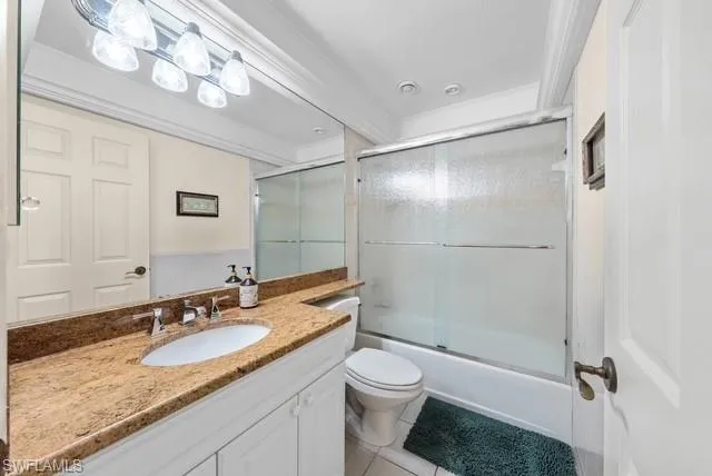 Bathroom with ornamental molding, vanity, light tile patterned floors, and combined bath / shower with glass door