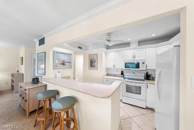 Kitchen featuring white appliances, a breakfast bar, white cabinets, light tile patterned floors, and ornamental molding