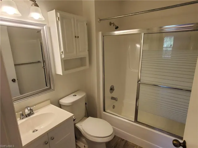 Full bathroom featuring wood-type flooring, combined bath / shower with glass door, vanity, and toilet