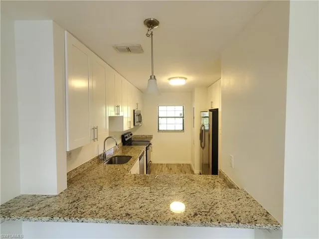 Kitchen featuring light stone countertops, light wood-type flooring, sink, white cabinetry, and appliances with stainless steel finishes