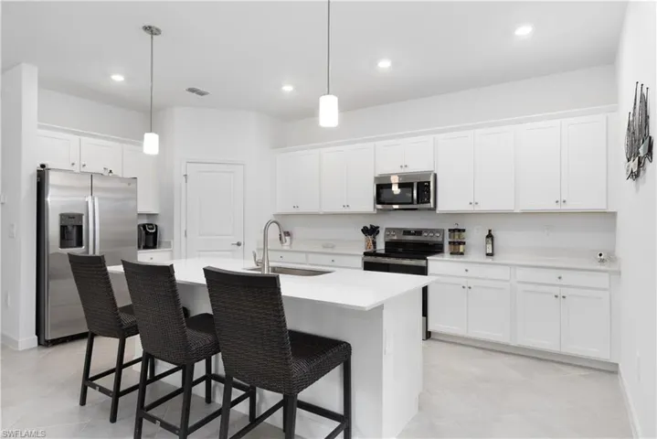 Kitchen featuring appliances with stainless steel finishes, hanging light fixtures, a kitchen breakfast bar, white cabinetry, and recessed lighting