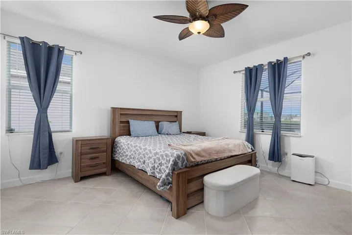 Tiled bedroom featuring a ceiling fan and multiple windows