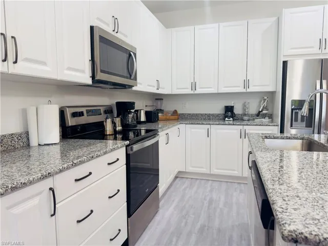 Kitchen with appliances with stainless steel finishes, white cabinetry, light stone countertops, and light wood-style flooring