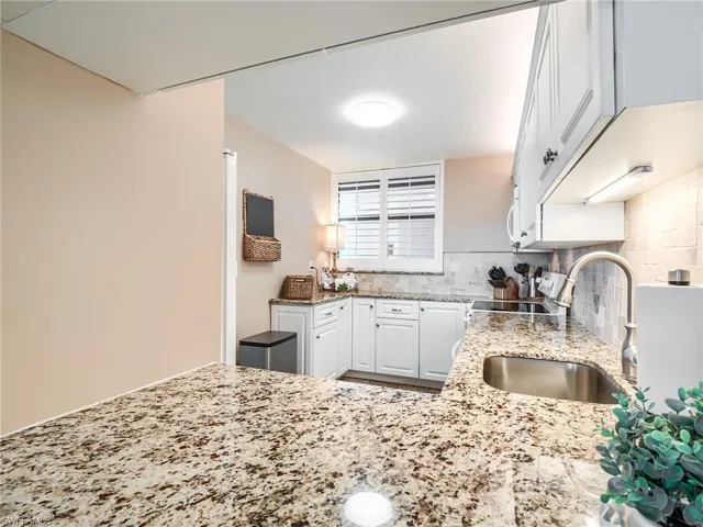 Kitchen with backsplash, sink, white cabinetry, and granite countertops updated in 2017