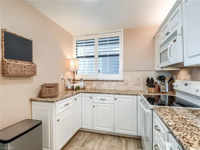 Kitchen featuring porcelain tile floors, white appliances, white cabinets, granite counters, and tasteful backsplash