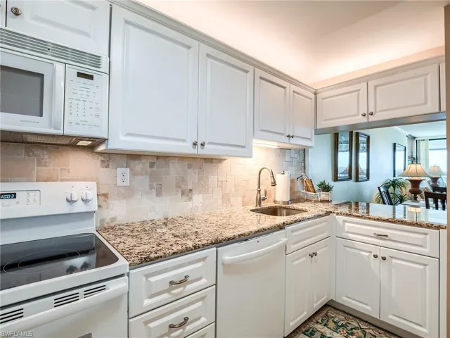 Kitchen with granite counters, tasteful backsplash, white cabinetry, newer sink, and white appliances