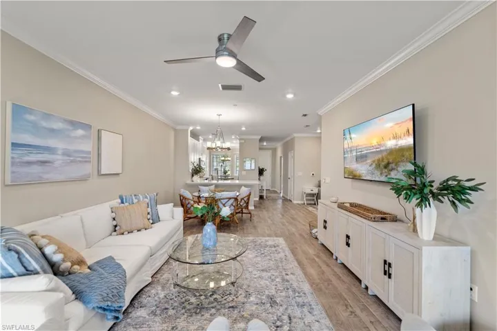 Living room featuring light hardwood / wood-style floors, ornamental molding, and ceiling fan with notable chandelier