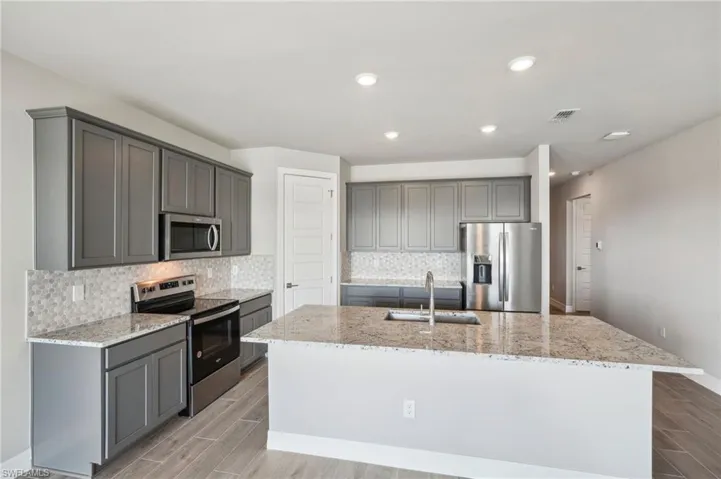 Kitchen with gray cabinetry, sink, a center island with sink, and appliances with stainless steel finishes