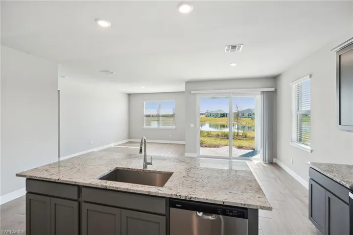 Kitchen featuring light stone counters, sink, stainless steel dishwasher, and a water view