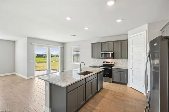 Kitchen featuring sink, appliances with stainless steel finishes, gray cabinets, a kitchen island with sink, and decorative backsplash