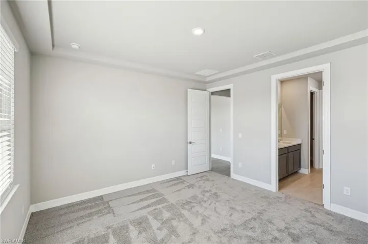 Unfurnished bedroom featuring multiple windows, connected bathroom, and light colored carpet