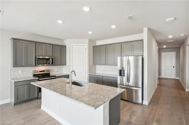 Kitchen with sink, light stone counters, an island with sink, stainless steel appliances, and decorative backsplash