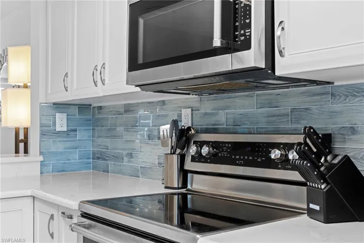 Kitchen featuring stainless steel appliances, white cabinetry, light stone countertops, and decorative backsplash