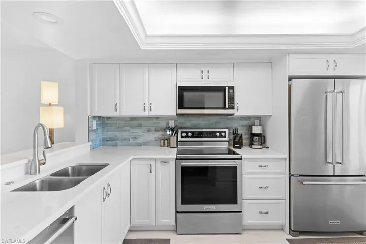 Kitchen featuring stainless steel appliances, white cabinetry, tasteful backsplash, and light stone countertops
