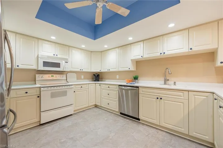 Kitchen with recessed lighting, stainless steel appliances, a tray ceiling, light countertops, and ceiling fan