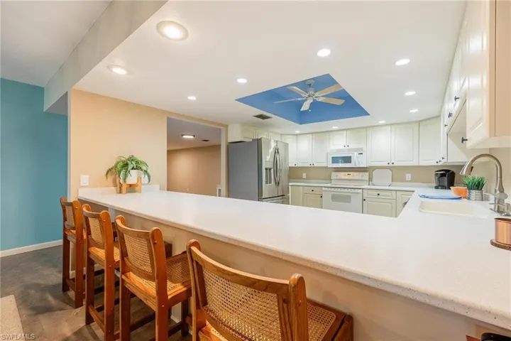 Kitchen featuring a breakfast bar, white appliances, a peninsula, recessed lighting, and light stone countertops