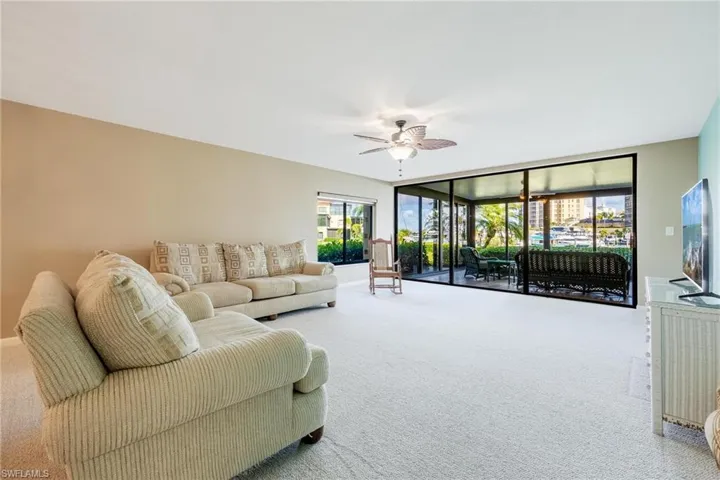 Carpeted living room with ceiling fan and a wall of windows