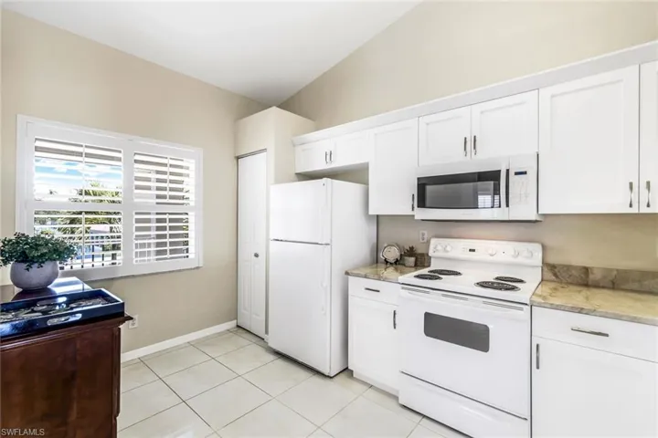 Kitchen featuring light tile patterned flooring, white appliances, vaulted ceiling, and white cabinets