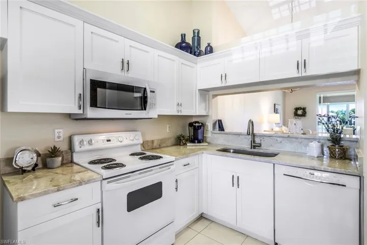 Kitchen with white appliances, white cabinets, sink, light stone counters, and light tile patterned floors