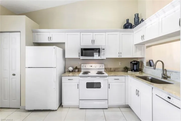Kitchen featuring white cabinets, vaulted ceiling, white appliances, and sink