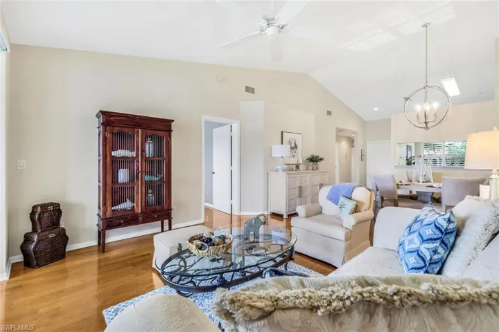 Living room with ceiling fan with notable chandelier, vaulted ceiling, and light wood-type flooring