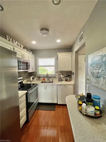 Kitchen with sink, appliances with stainless steel finishes, hardwood / wood-style floors, and white cabinetry