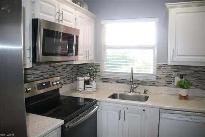 Kitchen featuring appliances with stainless steel finishes, white cabinetry, decorative backsplash, and sink