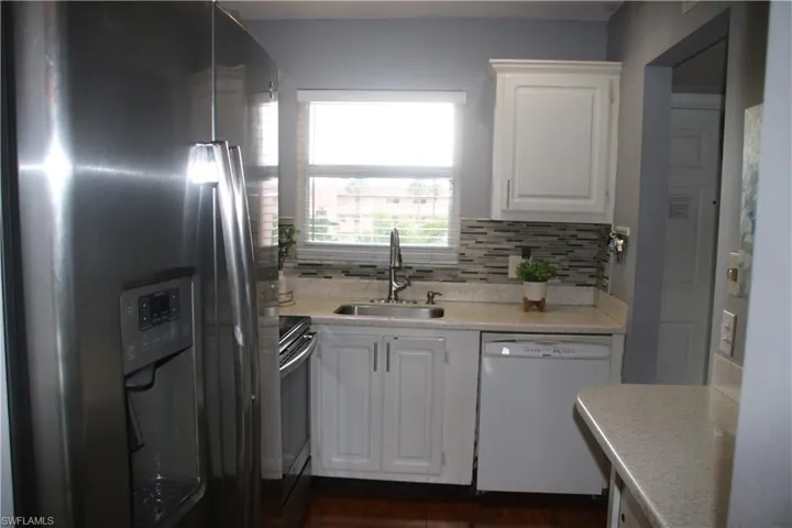 Kitchen with white cabinetry, dark hardwood / wood-style flooring, stainless steel appliances, decorative backsplash, and sink