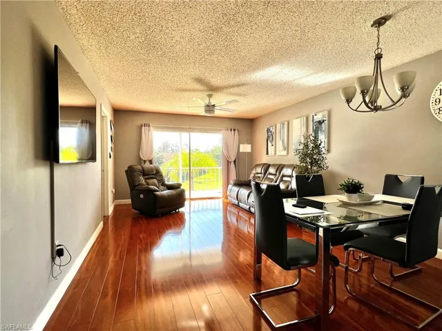 Dining space featuring ceiling fan with notable chandelier, wood-type flooring, and a textured ceiling