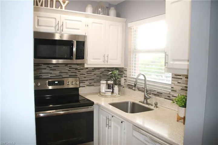 Kitchen featuring tasteful backsplash, white cabinets, light stone counters, appliances with stainless steel finishes, and sink