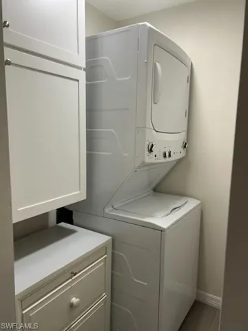 Laundry room with stacked washing maching and dryer, cabinets, and wood-type flooring