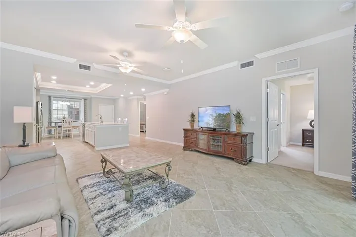 Spacious open-concept great room featuring volume ceilings, crown molding, large-format tile flooring, and seamless flow to the kitchen and dining areas.