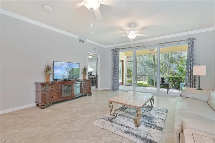 Spacious great room featuring volume ceilings, large-format tile flooring, and sliding glass doors that open to the screened lanai with peaceful preserve views.