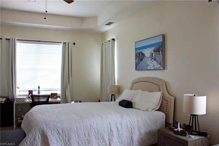 Recessed ceiling detail and neutral wall tones complement the ample natural light from the large window, complete with blinds and drapery