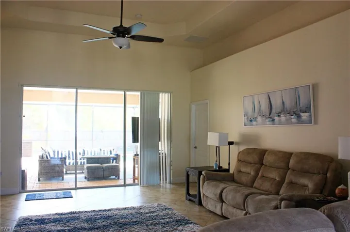 Vaulted tray ceiling with a ceiling fan, large sliding glass doors, screened patio, and tile flooring