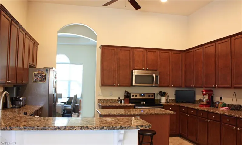 Kitchen featuring extensive wood cabinetry, granite countertops, an integrated kitchen island, stainless steel appliances, and an arched entryway