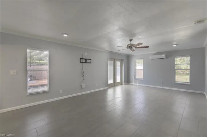 Tiled empty room featuring a wall mounted AC, ceiling fan, a textured ceiling, and ornamental molding