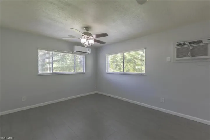 Empty room with a textured ceiling, ceiling fan, and a wall mounted air conditioner