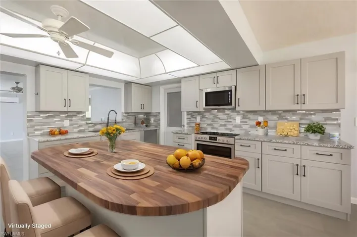 Virtually-staged Kitchen featuring a kitchen breakfast bar, decorative backsplash, wood counters, ceiling fan, and stainless steel appliances