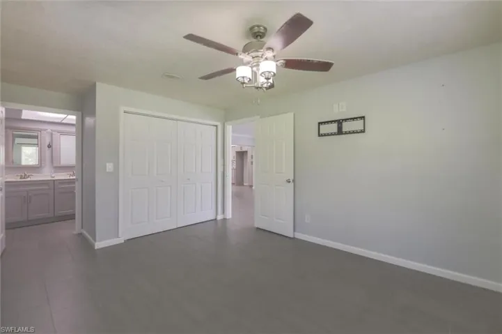 Unfurnished bedroom with ensuite bath, ceiling fan, a closet, and dark hardwood / wood-style flooring