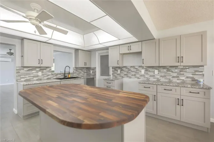 Kitchen with gray cabinetry, sink, butcher block counters, and tasteful backsplash