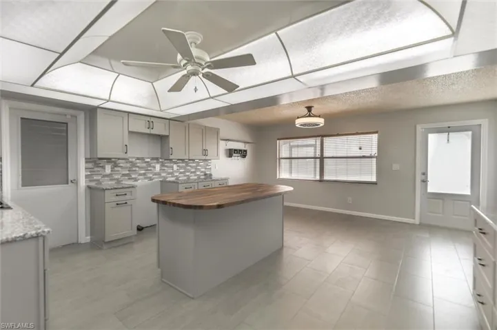 Kitchen with butcher block counters, ceiling fan, a center island, backsplash, and gray cabinets