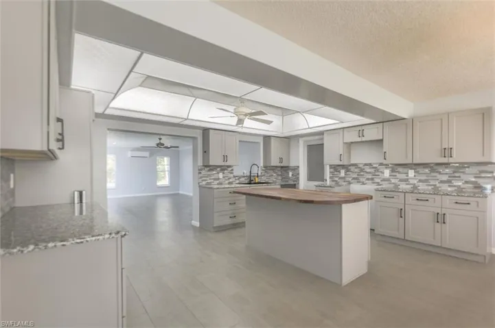 Kitchen featuring sink, decorative backsplash, ceiling fan, gray cabinets, and butcher block countertops