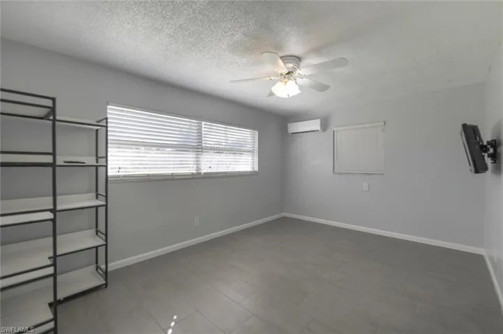 Unfurnished room with ceiling fan, a wall mounted AC, and a textured ceiling
